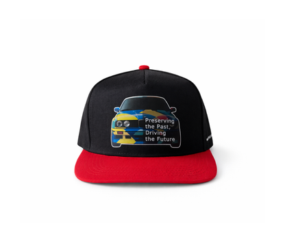Black and red cap with car graphic of BMW E30 and text Preserving the Past Driving the Future, vasarine kepure su E30